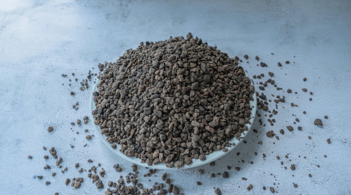 On a white table, a plate holds dark pumice stones, textured with porous surfaces and irregular shapes. Some stones rest scattered across the table, varying in size and shade, creating a rugged, natural arrangement of earthy elements.
