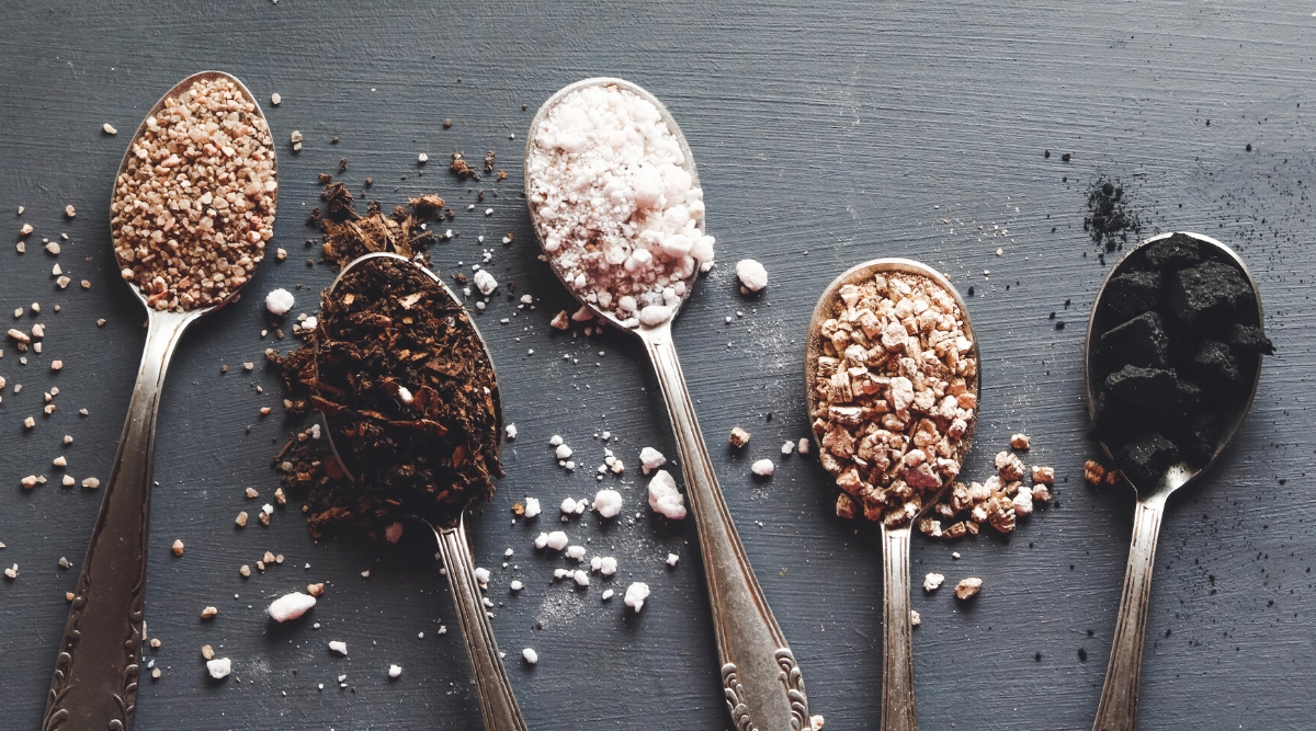 Five spoons, each filled with a different type of succulent soil fertilizer. Each spoon contains a different type of succulent soil fertilizer: perlite, vermiculite, compost, coarse sand, and charcoal. The scene evokes a miniature landscape ready to nourish tiny desert gems.
