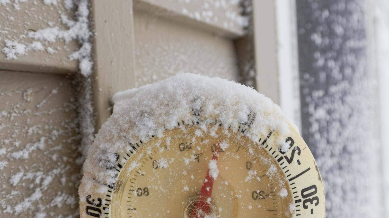 Close up view of a snow-capped thermometer mounted on the wooden siding of a house showing freezing temperatures